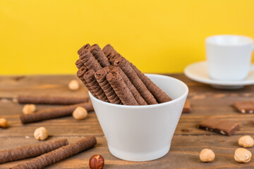 Tasty rolled wafer cookies with hazelnuts and chocolate pieces on wooden table