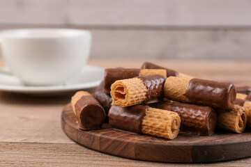 Tray with delicious wafer rolls and cup on wooden table
