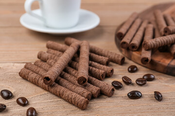 Tray with tasty rolled wafer cookies, coffee beans and cup on wooden background