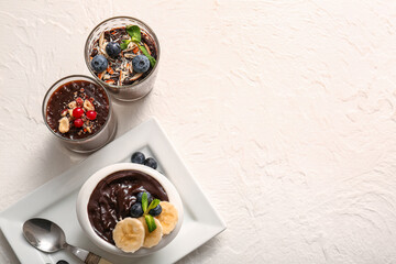 Glasses and bowl with delicious chocolate pudding, berries, nuts and banana on white table