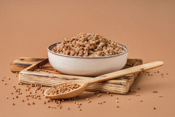 Board with bowl of tasty buckwheat porridge on beige background