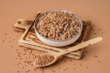 Board with bowl of tasty buckwheat porridge on beige background