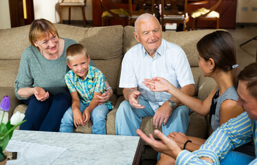 Smiling senior woman and man talking to their children and grandson while sitting on sofa at home..