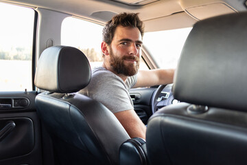 Taxi app driver smiling while turning over to the backseat looking talking with client 