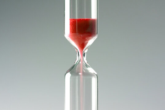 Deadline, time limit, remaining, or bleeding (losing something critical or necessary), concept background image. Red sand of hourglass or sand clock falling down.