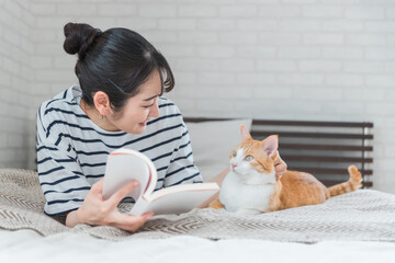 家のベッドルームでペットの猫と遊ぶアジア人女性(読書・スキンシップ)
