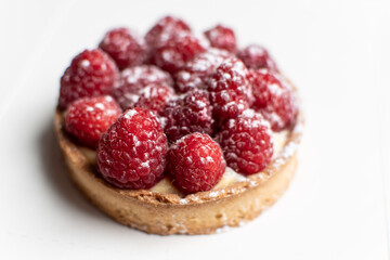 Raspberry and custard tartlet. Delicious French pastry tart. Select focus on two raspberries in the front. White background.