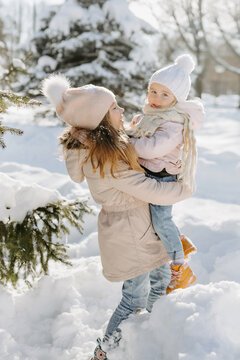 Portrait of young girl holding on hands her little sister while standing among piles of snow. Happy children, enjoying of cold weather at the park during winter vacation