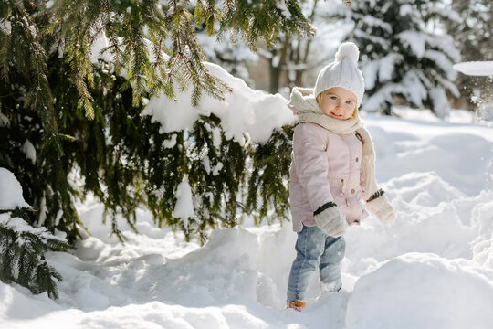 Portrait of a cute little girl posing alone in a snowy park. Happy child, standing near snowy twig of Christmas tree and looking at camera