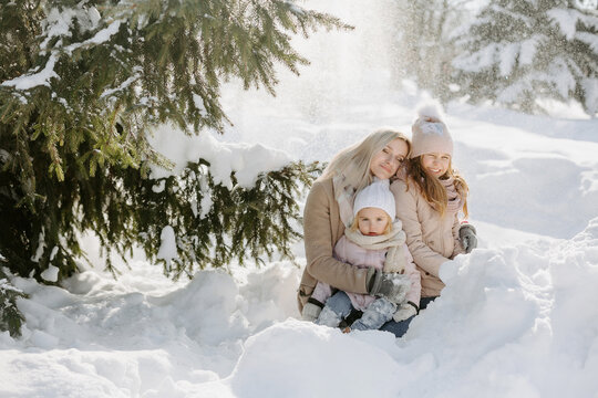 Portrait of tender mother with children enjoying snowfall in forest. Loving mum, with long hair, embracing daughters while spending winter holidays together at park