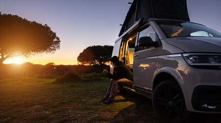 man sitting with digital device at his Transporter Camping Van bus at the California Ocean in the...