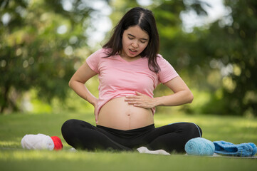 Fototapeta na wymiar Asian pregnant woman suffering from abdominal pain in the garden