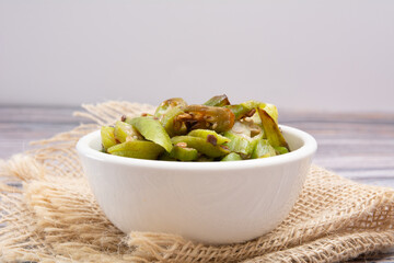 Grilled okra, in a white bowl on a wooden table, focused, front view