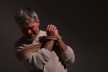 Emotional victim tied with rope on dark background, space for text. Hostage taking