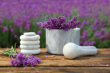 Spa stones, fresh lavender flowers and white marble mortar on wooden table outdoors, closeup