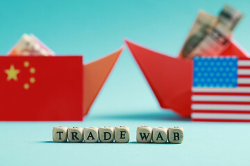 Phrase Trade war made of wooden cubes near paper boats with money and national flags on turquoise background