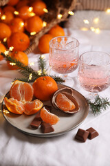 Delicious ripe tangerines, chocolates, festive lights and glasses of wine on white bedsheet