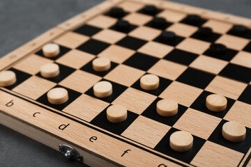 Wooden checkerboard with game pieces on grey table, closeup