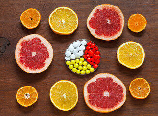 Vitamins natural from citrus fruits and synthetic in form of medicinal tablets on wooden background. Health care concept. Improving immunity and taking vitamins in cold season. Flat lay, close-up