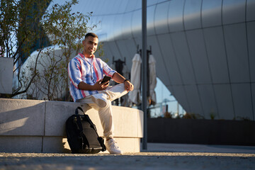 Young Iranian man holding smartphone and looking at the camera at the city. Handsome young guy in...