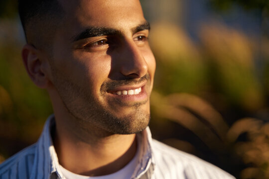 Closeup portrait of handsome smiling middle eastern man  looking away enjoying sunset in park  