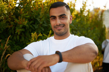 Portrait of happy handsome middle eastern man in casual clothes looking at camera relaxing in park 