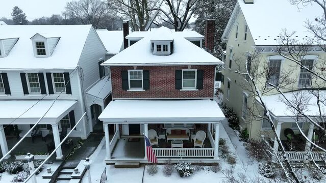 Rising aerial of snow covered home with American flag waving on front porch. Patriotic American citizen in small town in USA.