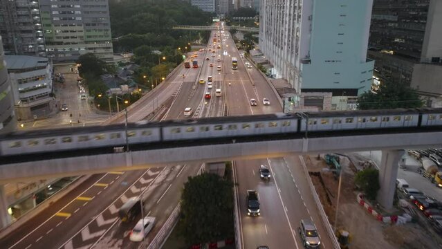 Aerial backwards shot -  traffic on road and train passing on bridge. Kwai Chung, Hong Kong, at sunset time