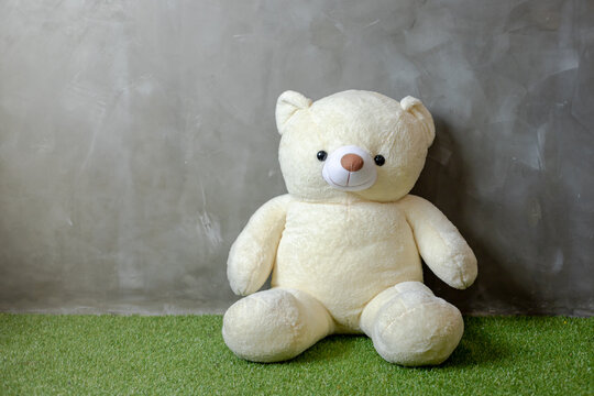 Cute yellow teddy bear sitting on artificial grass cement wall background child concept