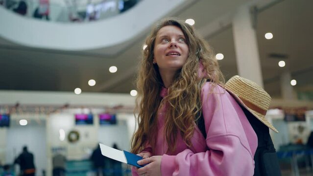 Pretty girl holding a ticket in abroad passport at the airport smiling and looking around. Young female tourist Traveling concept