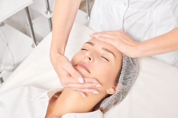 Cosmetologist massages woman face skin after rubbing moisturizing cream for rejuvenation, anti...