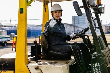 Middle-aged Asian male worker with forklift on factory grounds.
