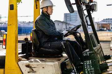 Middle-aged Asian male worker with forklift on factory grounds.