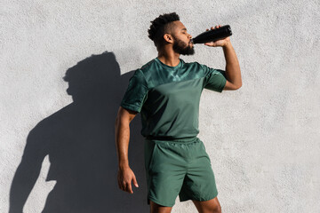 Tired thirsty Black male athlete drinking water outdoor fitness workout