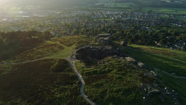 Establishing Drone Shot with Rays of Sun of Hangingstone Rocks Rock Formation on Ilkley Moor with Ilkley Town in Valley at Golden Hour Sunset UK
