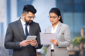 Indian businessman and businesswoman using digital tablet on city street.