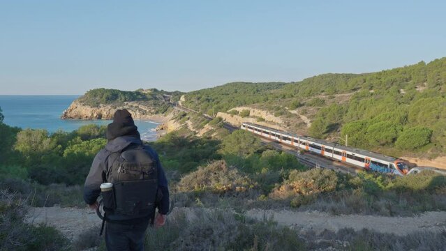 landscape with the sea far away, train in distance leaving and cyclist walks towards his bike leaving the sunny mountainous scene