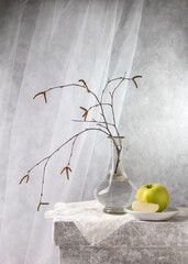 Modern still life with a birch branch in a glass vase and a green apple on a light background