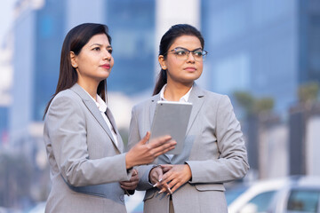 Two businesswomen working on a tablet outdoors.