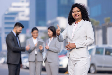 Young business woman pointing okay, behind her colleagues discussing.