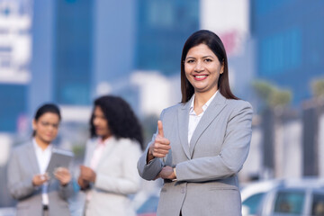 Obraz premium Young business woman pointing okay, behind her colleagues discussing.