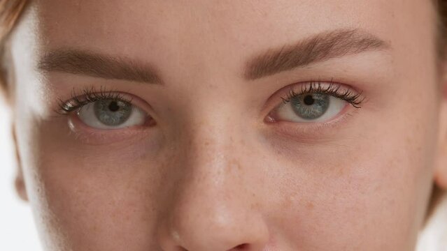 Extreme close-up shot of good-looking young brown-haired Caucasian woman opens her eyes and looks at the camera on white background | Eye care products commercial