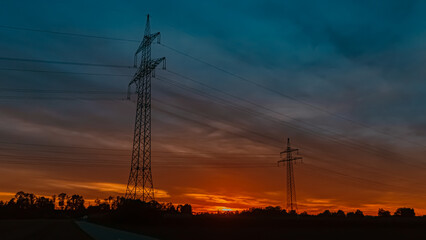 Beautiful sunset with a dramatic sky and overland high voltage lines near Tabertshausen, Bavaria, Germany