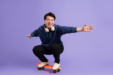 Image of young Asian man playing skateboard on purple background