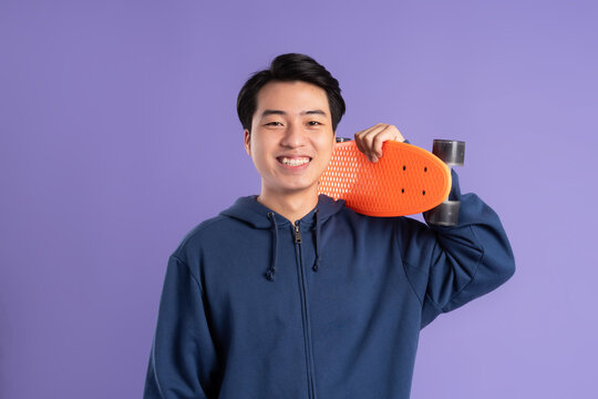 Image of young Asian man playing skateboard on purple background