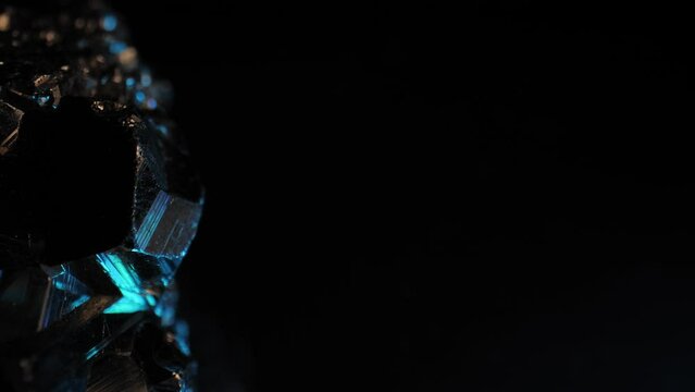Pyrite crystal shimmering in blue light against dark background. Cinematic smooth pan and macro lens for intricate details.