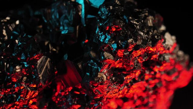 Vibrant detailed shot of golden pyrite crystal aglow against dark background, lit by red and blue lights. Smooth pan and macro lens.