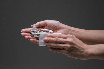 Lady hand applying alcohol wipe hand sanitiser towards the earpiece to prevent the spread of bacteria and virus. Personal hygiene concept. Isolated black background