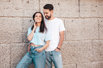 Obraz na płótnie Canvas Smiling beautiful woman and her handsome boyfriend. Woman in casual summer jeans clothes. Happy cheerful family. Female having fun. Sexy couple posing in the street near wall