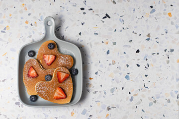 Heart shaped pancakes for romantic breakfast served with strawberry, blueberry and powdered sugar. Valentine's Day concept. Terrazzo background. Top view. Love and hearts theme. Copy space